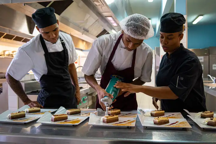 Une monitrice du RSMA guide un volontaire pendant le dressage de desserts en cuisine
